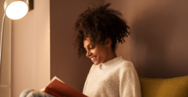 A photo of a woman reading near a lamp. 